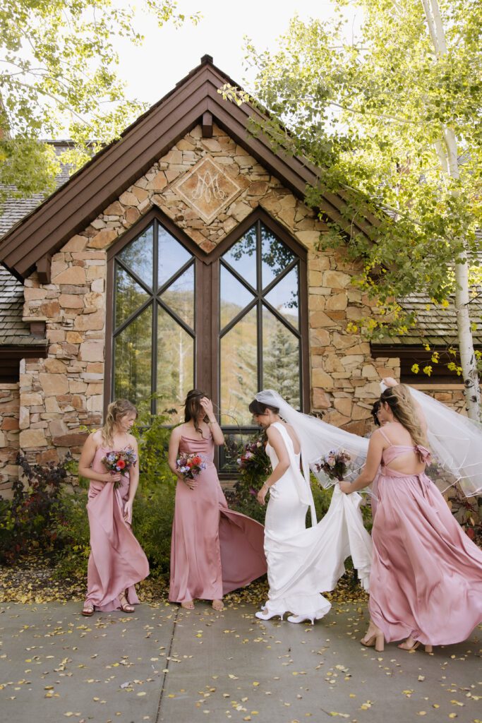 bride walking with her best friends in front of the church while they help with her wedding dress after the ceremony featuring stunning fall colors.