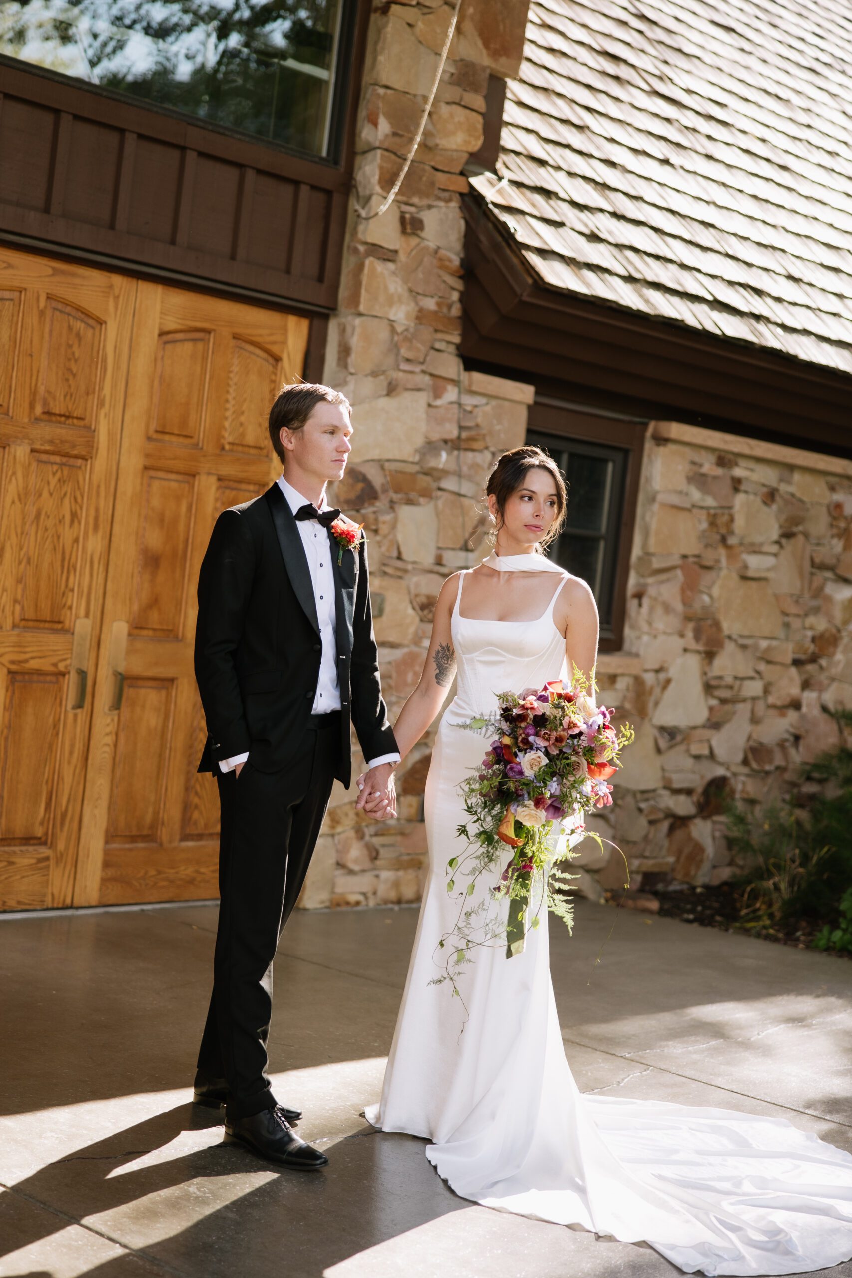 bride and groom standing in front of the church where they just got married looking off holding hands side by side