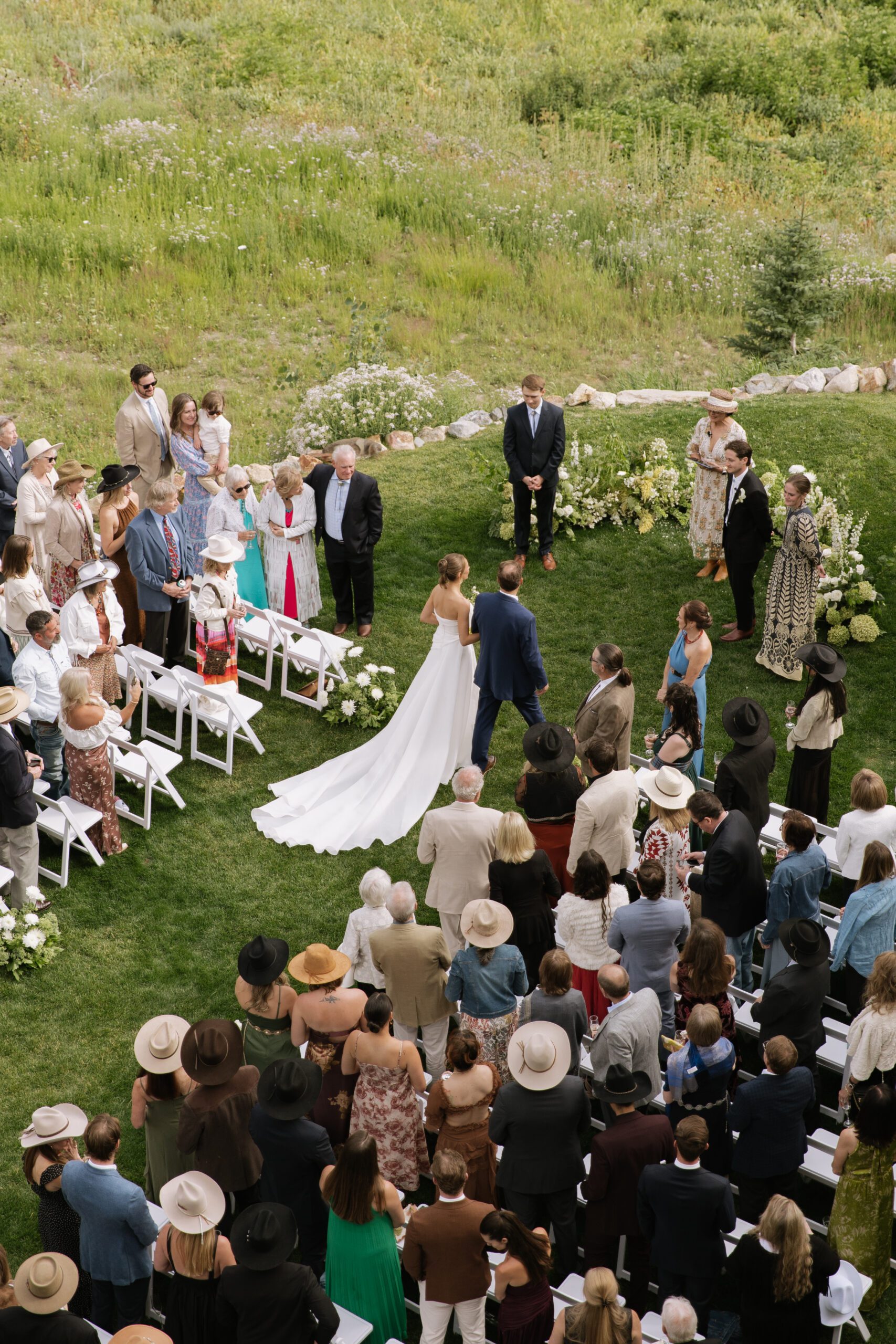 S and P at their outdoor wedding ceremony at Alta’s Rustler Lodge with white flowers and green Utah mountains behind them.