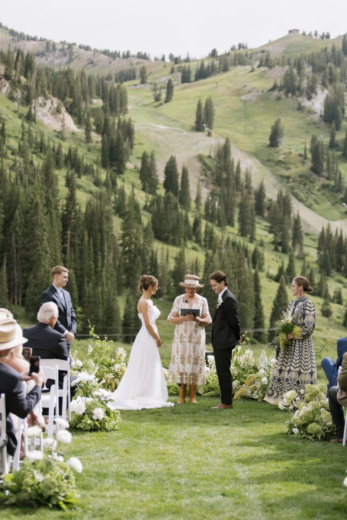 S and P during their Alta’s Rustler Lodge wedding ceremony with green mountains behind them.
