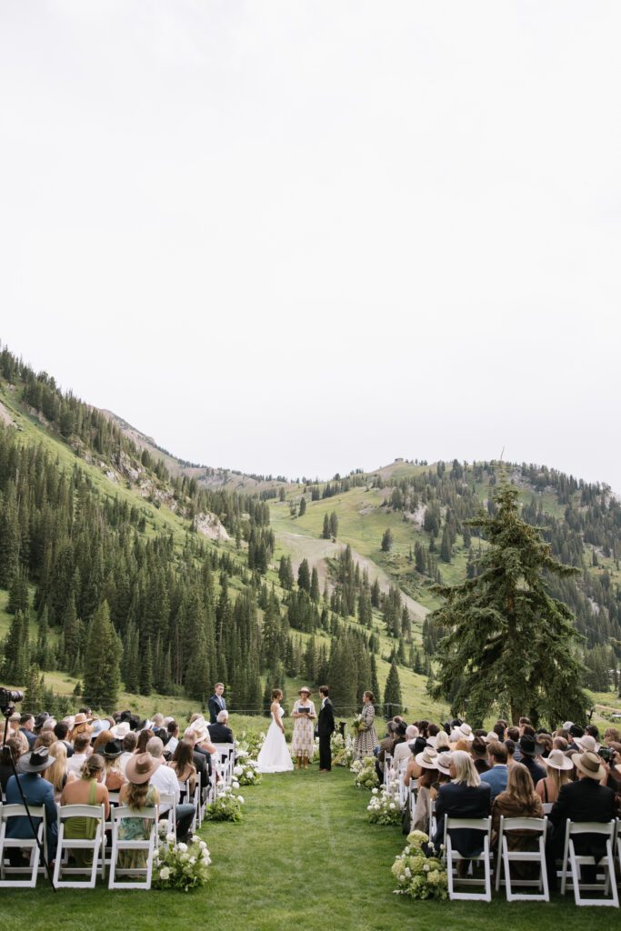 S and P during their Alta’s Rustler Lodge wedding ceremony with green mountains behind them.