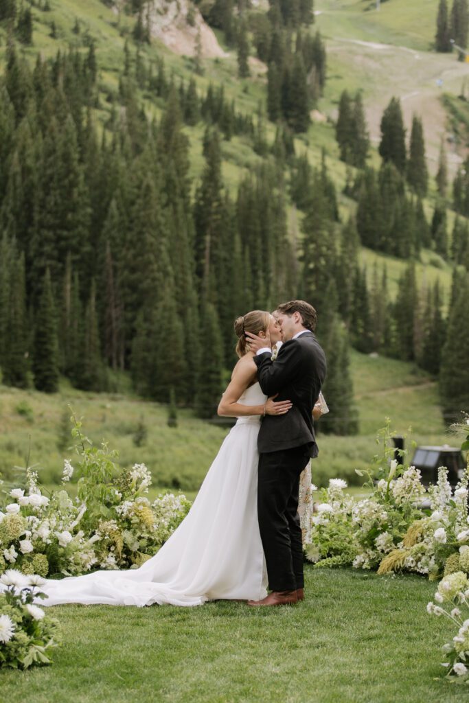S and P during their Alta’s Rustler Lodge wedding ceremony with green mountains behind them.