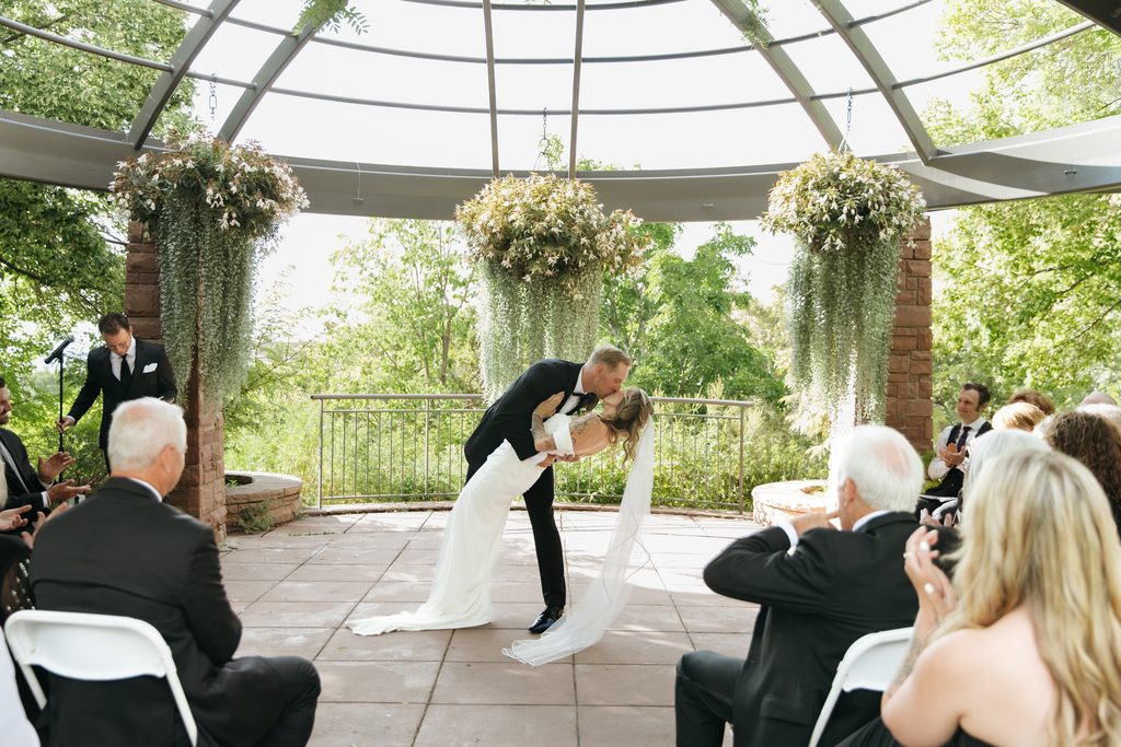 A and M kissing kissing after ceremony at Red Butte Garden, surrounded by greenery.