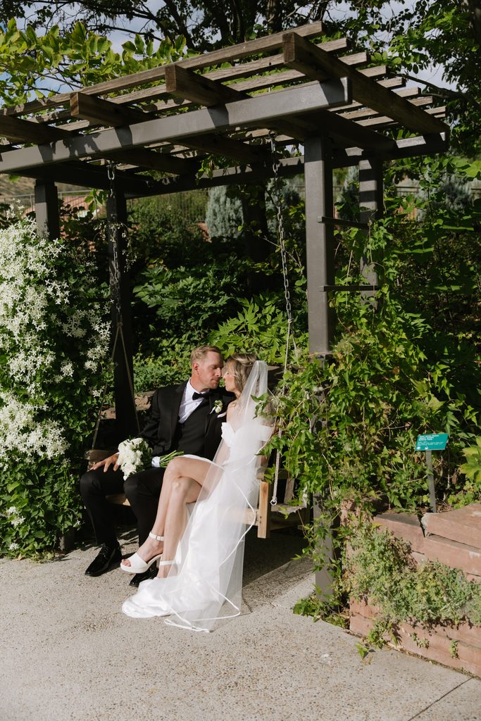 A and M sitting on a garden swing at Red Butte Garden, surrounded by greenery and white flowers.
