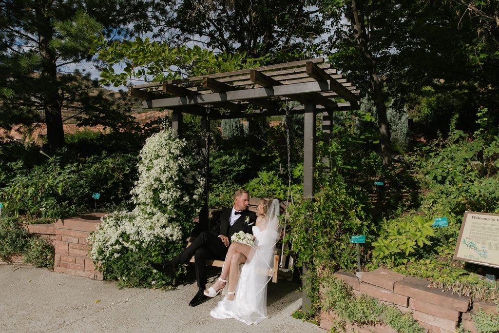 A and M sitting on a garden swing at Red Butte Garden, surrounded by greenery and white flowers.
