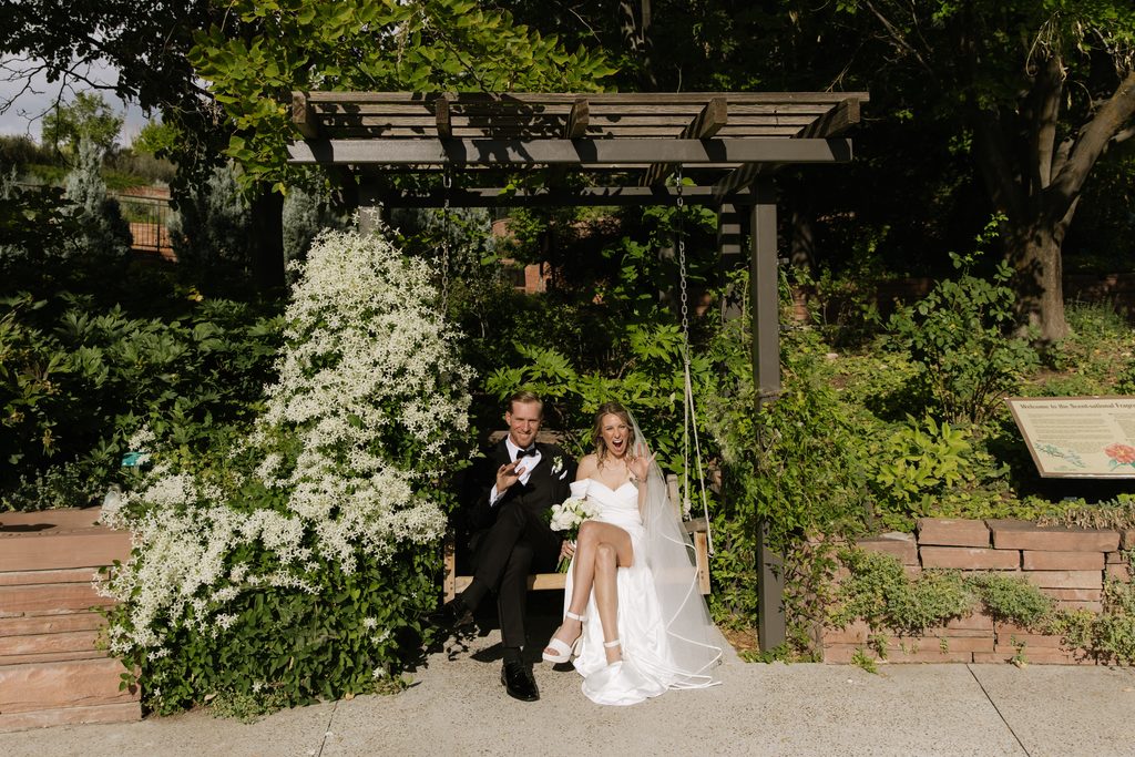 A and M sitting on a garden swing at Red Butte Garden, surrounded by greenery and white flowers.